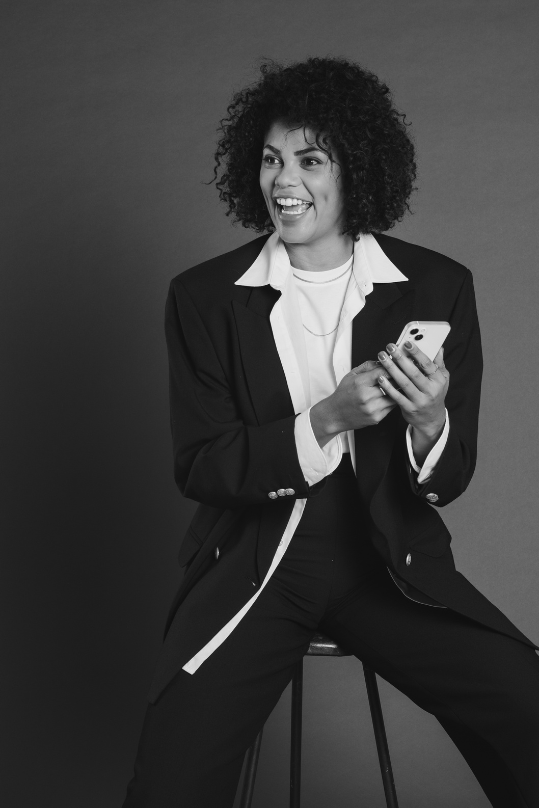 Smiling Woman Sitting on a Chair and Using a Smartphone